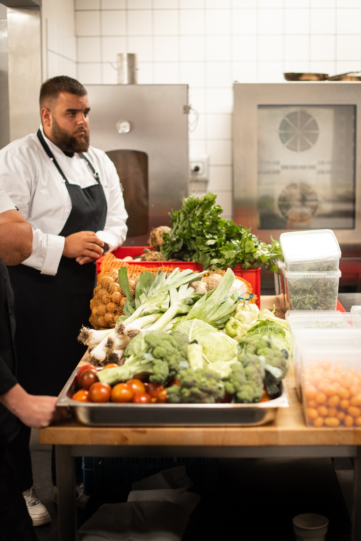 Šéfkuchař v kuchyni se sezonní zeleninou připravovanou na degustační menu – pórek, brokolice, rajčata, zelí a další čerstvé suroviny.