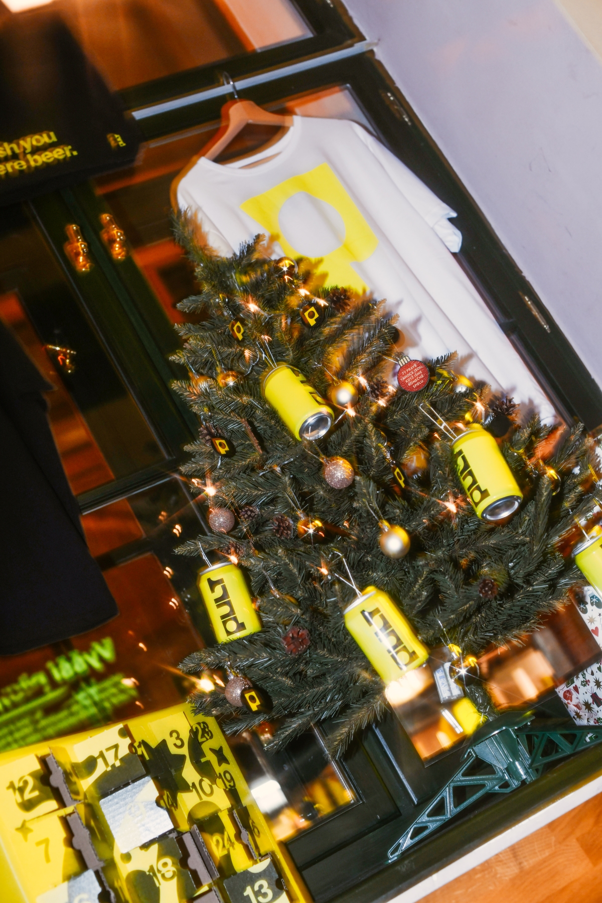 Vánoční stromek zdobený žlutými plechovkami Pultu a firemními ozdobami u okna.