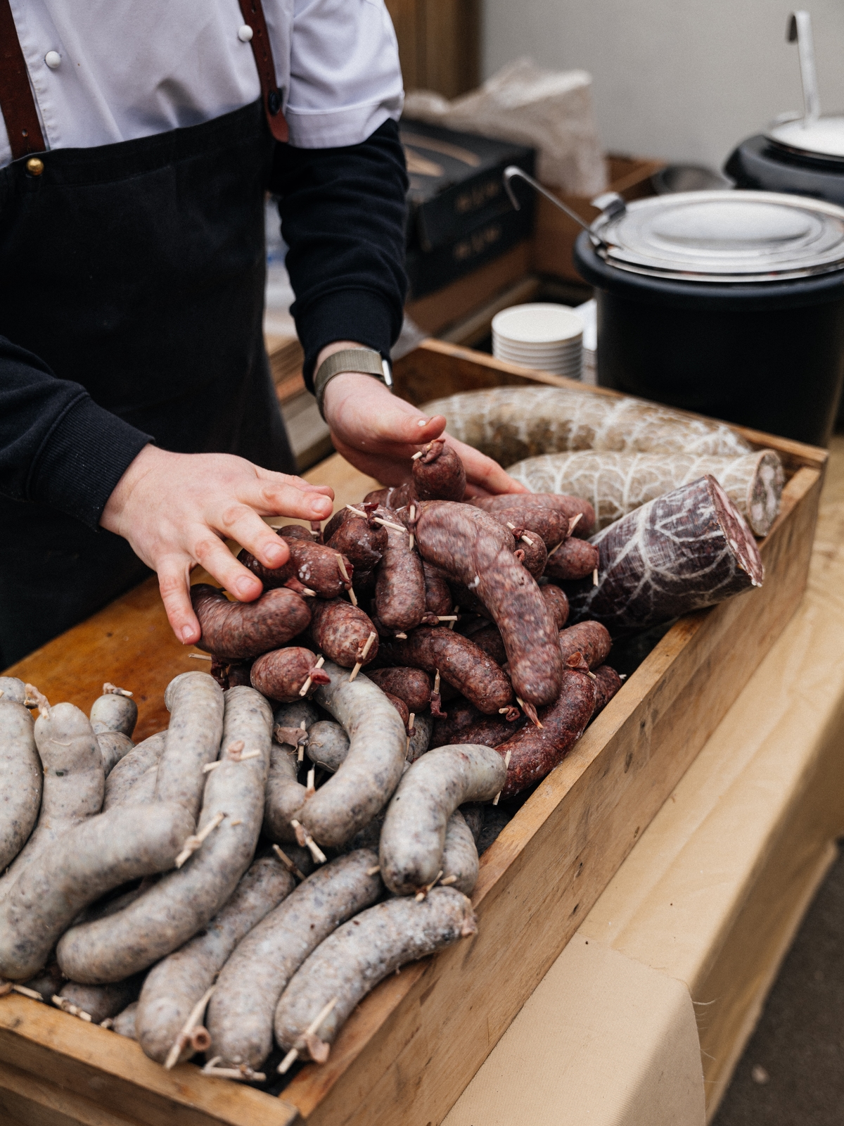 Kuchař aranžuje klobásy a jitrnice ve dřevěné bedýnce.